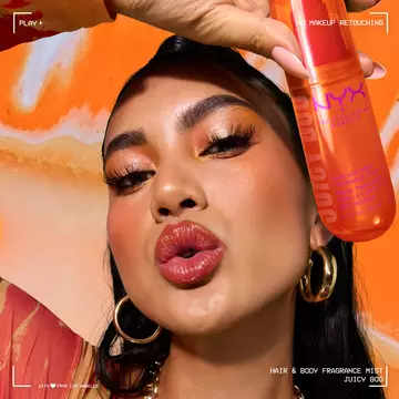 Model in warm orange tones holding NYX Professional Makeup Juicy Boo Hair & Body Fragrance Mist on orange/magenta background.
