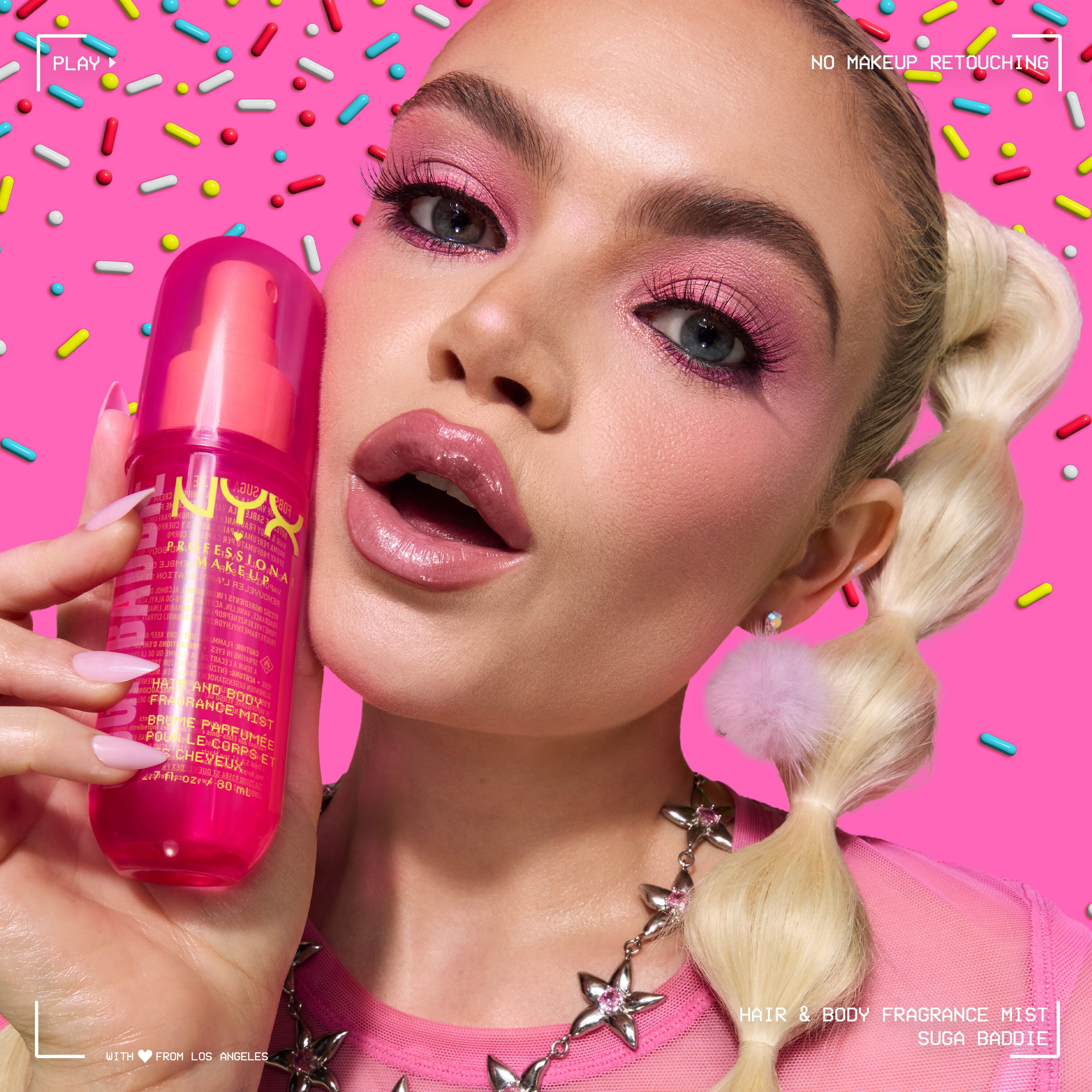 Lifestyle shot of model with dramatic pink eye makeup holding NYX Professional Makeup Suga Baddie Hair & Body Fragrance Mist pink bottle.