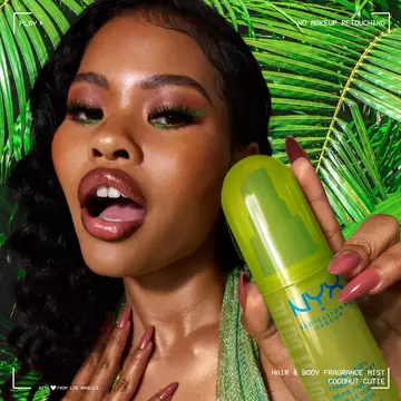 Lifestyle shot of model holding lime green Coconut Cutie Hair & Body Mist with palm leaves in the background.