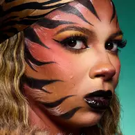 NYX Professional Makeup tiger Halloween look with orange face paint, black tiger stripes, gold eye makeup and glossy black lips.