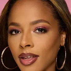 Model wearing NYX Make ’Em Wonder™ Foundation in shade 26 Honey with deep mauve lips and gold hoop earrings.