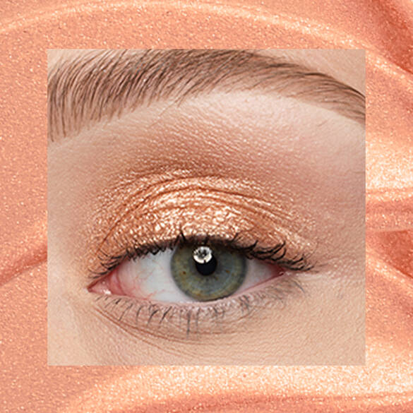 Close-up of a fair-skinned eye wearing 05 Gold String, a peachy gold metallic cream eyeshadow from NYX Professional Makeup Lid Lingerie, on a matching peach-gold shimmer backdrop.