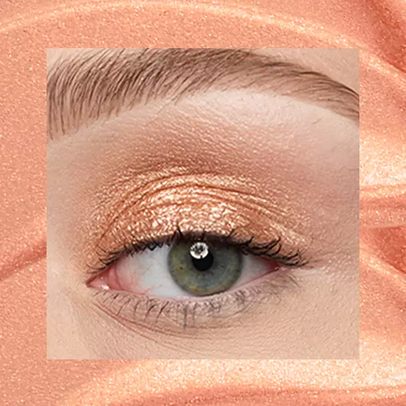 Close-up of a fair-skinned eye wearing 05 Gold String, a peachy gold metallic cream eyeshadow from NYX Professional Makeup Lid Lingerie, on a matching peach-gold shimmer backdrop.