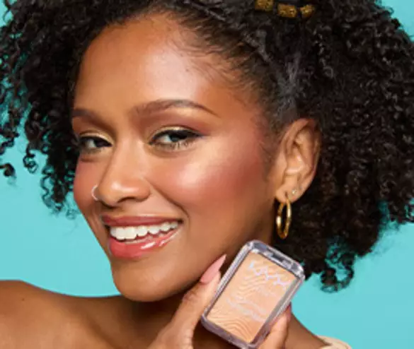 Smiling model looking at the camera and holding Buttermelt Highlighter in shade 30 Butta Bling