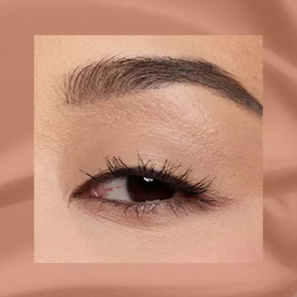 Close-up of a fair-skinned eye wearing 03 Beige Appeal, a warm beige matte cream eyeshadow from NYX Professional Makeup Lid Lingerie, on a matching beige matte backdrop.