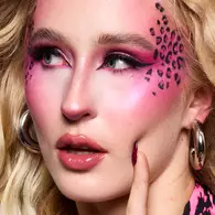 NYX Professional Makeup pink leopard-inspired Halloween look with bright pink eyeshadow, glossy pink lips and black leopard spots across the cheek.