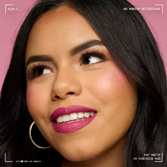 Close-up of model with medium skin tone wearing NYX Professional Makeup Fat Matte Smooth Color Lipstick in Hibiscus Hug, a magenta shade, showing a smooth, non-cakey matte finish. No makeup retouching.
