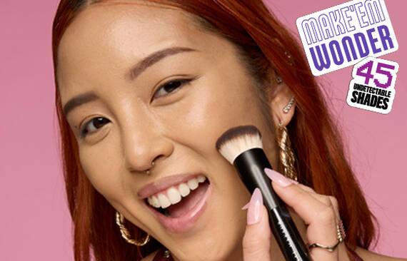 Model applying NYX Make ’Em Wonder™ Foundation with brush, text overlay Make ’Em Wonder™ 45 Undetectable Shades.