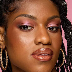 Model wearing NYX Make ’Em Wonder™ Foundation in shade 32 Cappuccino with glossy lips and pink shimmer eyes.