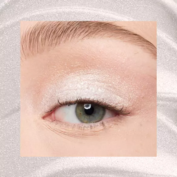 Close-up of a fair-skinned eye wearing 01 Satin Silver, an ice-white metallic cream eyeshadow from NYX Professional Makeup Lid Lingerie, on a matching silver shimmer backdrop.