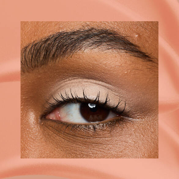 Close-up of a deep-skinned eye wearing 02 In-Nude-Endo, a peachy nude matte cream eyeshadow from NYX Professional Makeup Lid Lingerie, on a matching peach matte backdrop.