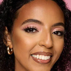 Model wearing NYX Make ’Em Wonder™ Foundation in shade 27 True Caramel with pink eyeshadow and glossy lips.