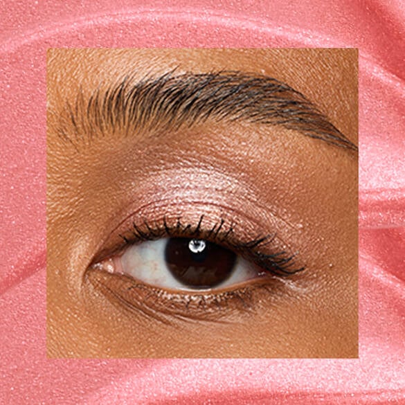Close-up of a deep-skinned eye wearing 04 Risky Rose, a rose-gold metallic cream eyeshadow from NYX Professional Makeup Lid Lingerie, on a matching pink-rose swatch backdrop.