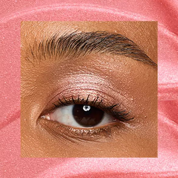 Close-up of a deep-skinned eye wearing 04 Risky Rose, a rose-gold metallic cream eyeshadow from NYX Professional Makeup Lid Lingerie, on a matching pink-rose swatch backdrop.