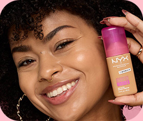 Close-up of model posing and smiling while holding Make 'Em Wonder™ Foundation in shade 17 Medium Olive