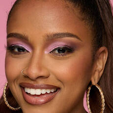 Model wearing NYX Make ’Em Wonder™ Foundation in shade 28 Cinnamon with glowing finish and pink shimmer eyes.