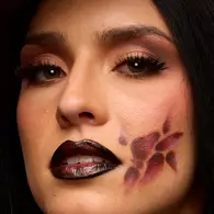 NYX Professional Makeup orange and black Halloween look with a large graphic eye design painted across the face and glossy black lips.