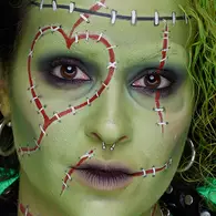 NYX Professional Makeup green stitched-face Halloween look with green skin paint, red stitched lines, dark eyes and black lips.
